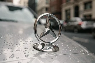 Gros plan sur l'emblème étoile à trois branches de Mercedes-Benz sur le capot d'une voiture de luxe, avec des gouttelettes d'eau sur le chrome poli